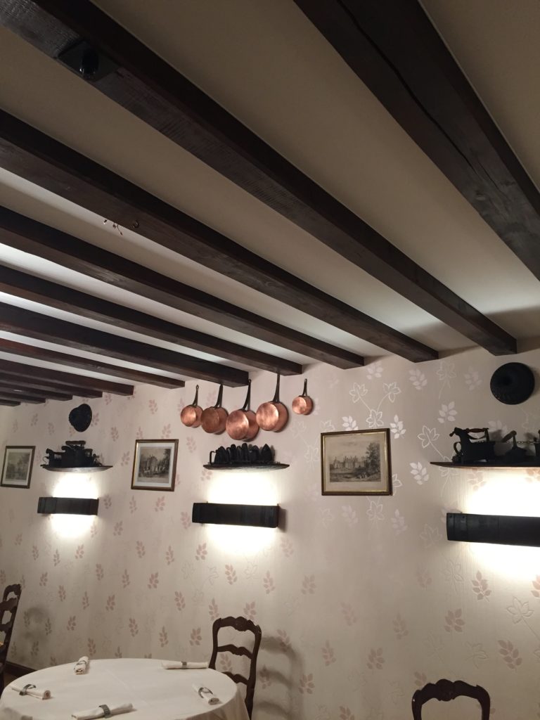 Vue d'un plafond acoustique blanc entre poutres dans une salle de l'Auberge Au vieux Presoir