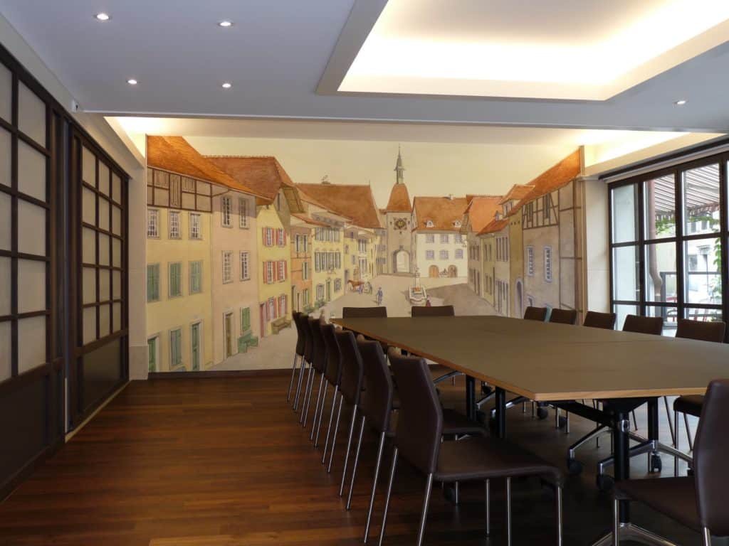 Photo d'une salle de séminaire dans un hôtel avec un mur imprimé à partir d'une aquarelle représentant la place du village