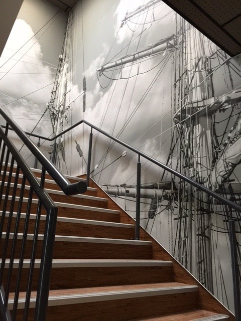 Photo d'un mur imprimé dans une montée d'escalier acec un visuel de mâts de bateau