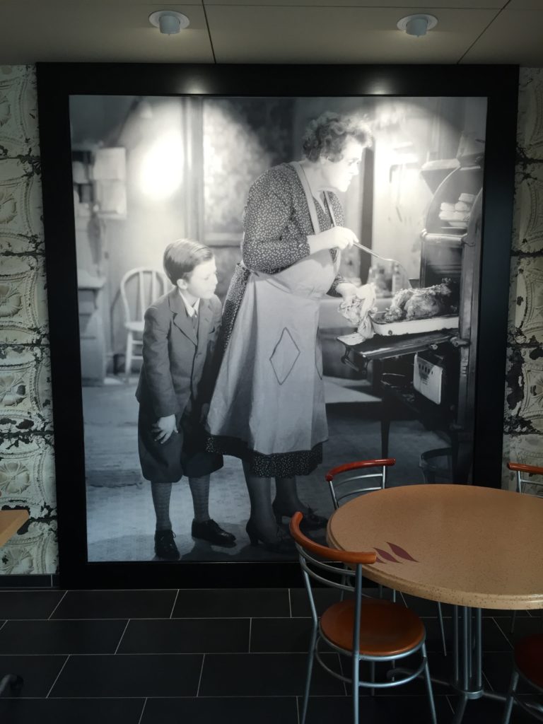photo d'un mur imprimé en n&b avec une photo d'une femme sortant un poulet du four et de son petit-fils qui la regarde