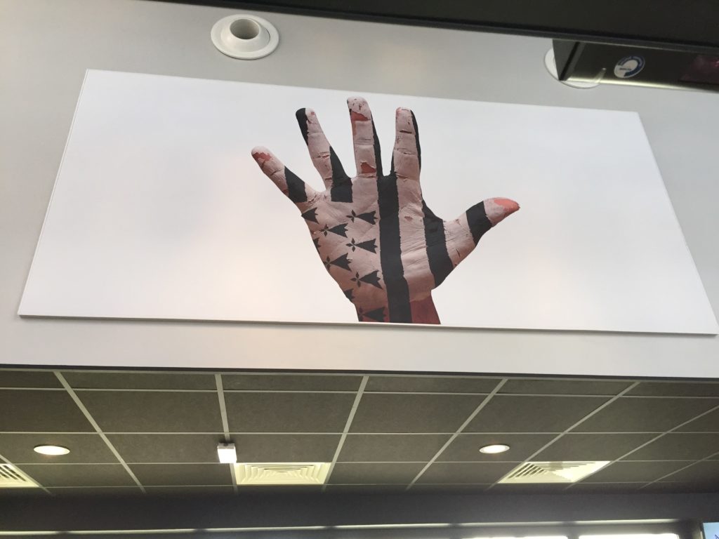 Photo d'un mur imprimé avec un visuel de mains sur laquelle est peinte le drapeau breton