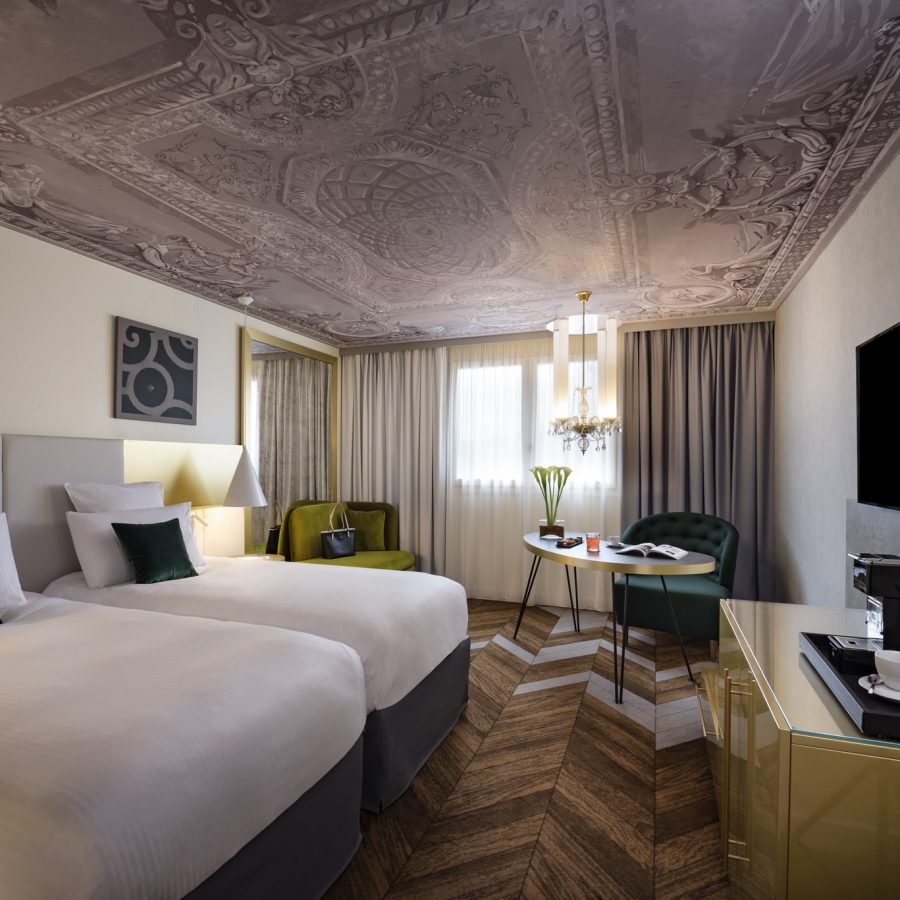 Plafond en toile imprimé ALYOS design Photo du plafond d'une des chambres de l'Hôtel Le Louis avec un visuel représentant une peinture d'un plafond avec moulures